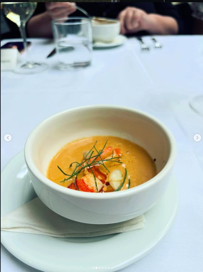 An orange soup in a white bowl with a delicate garnish